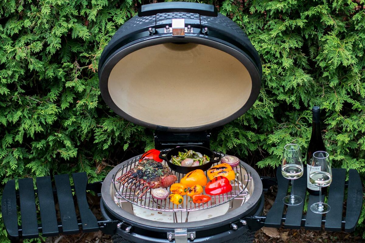 Kamado 25 in a backyard patio with its lid open revealing vegtables and grilled lamb.